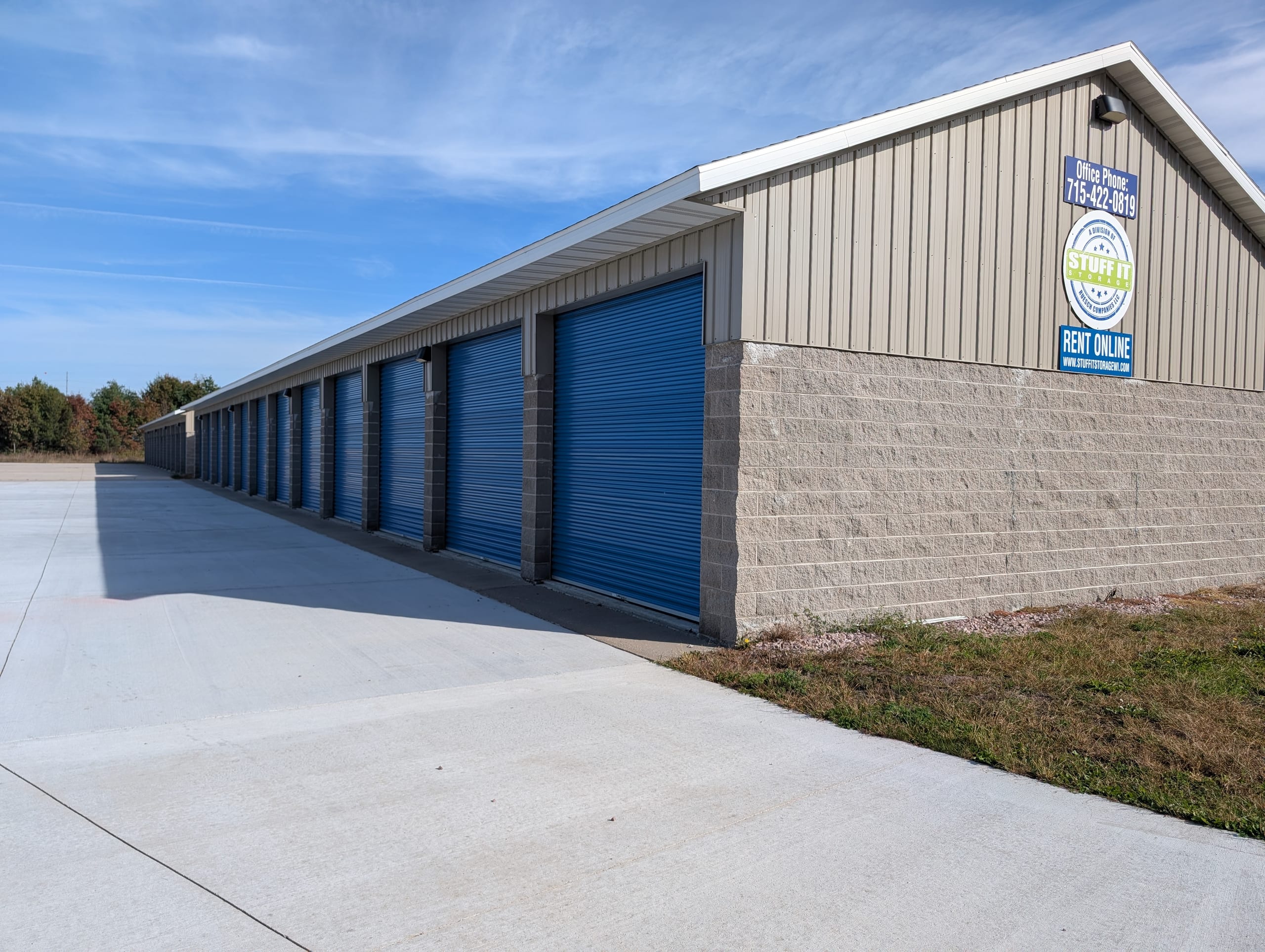 Evergreen storage building with a block base, a long row of blue roll-up doors and Stuff it Storage signs