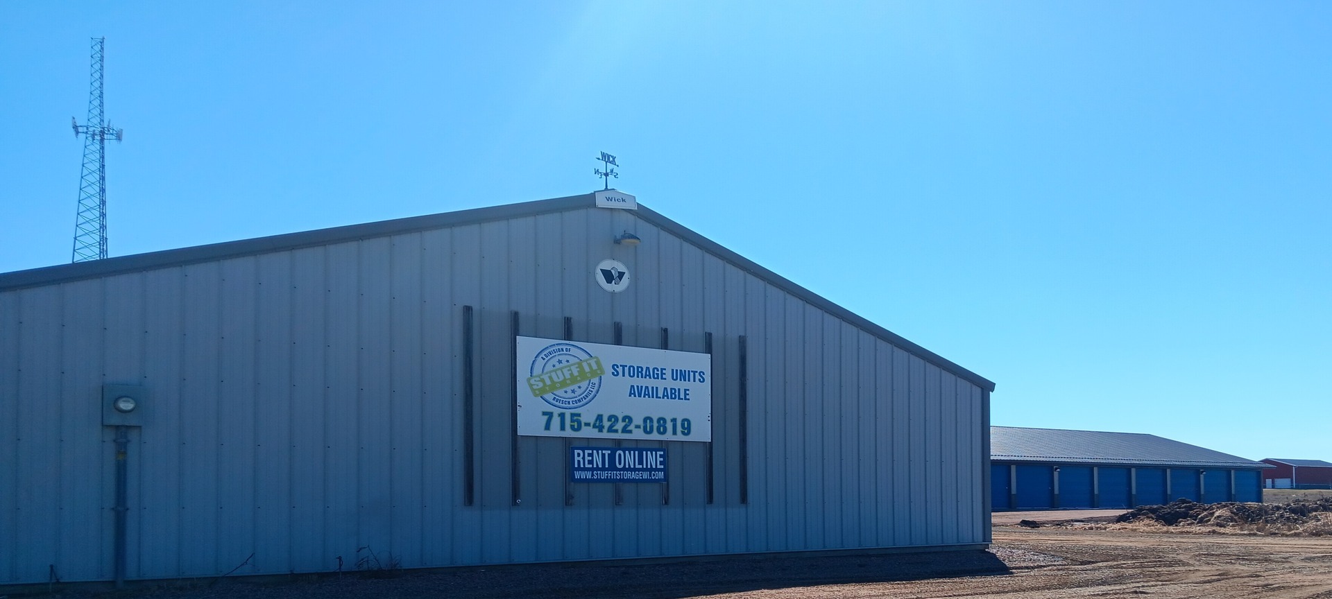 Rudolph storage building with a Storage Units Available sign and blue-door units behind it